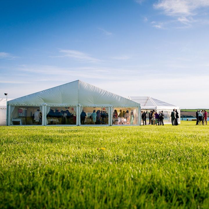 A group of people are standing in a grassy field in front of a large tent.