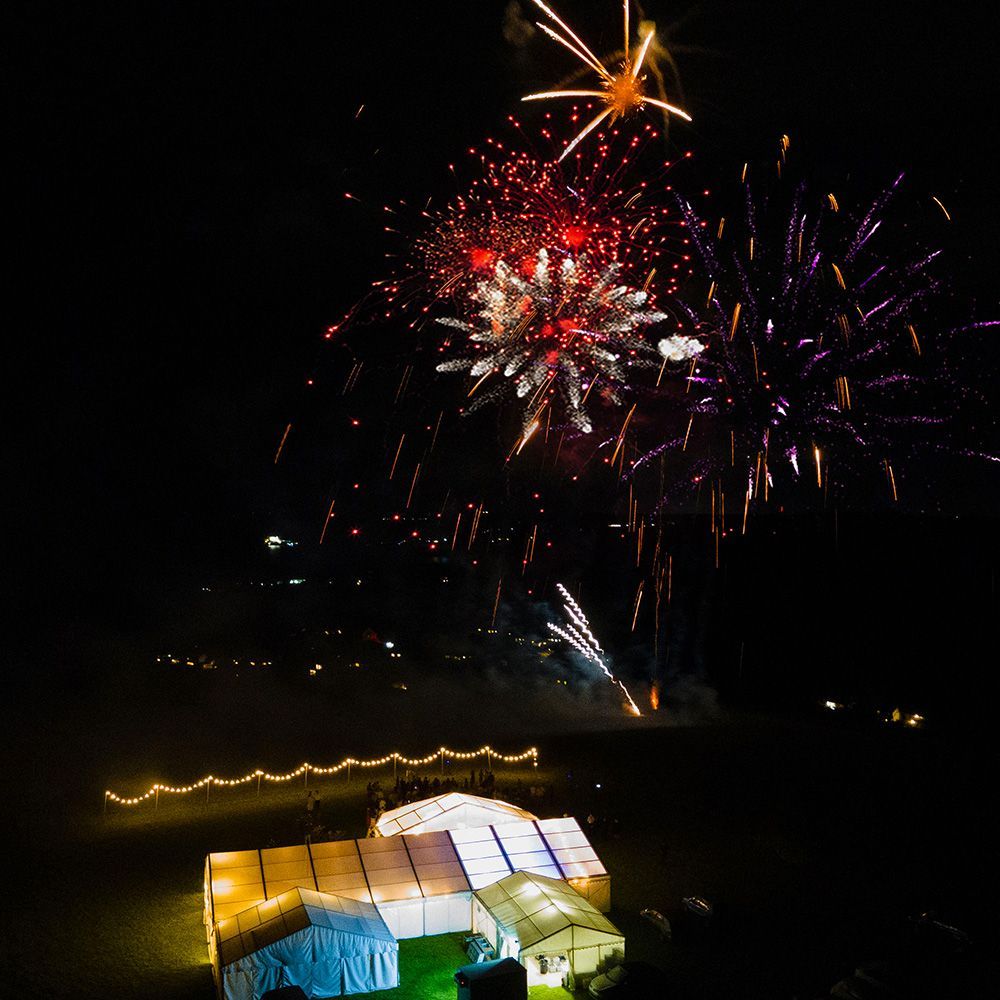 A group of people watching fireworks over a tent at night