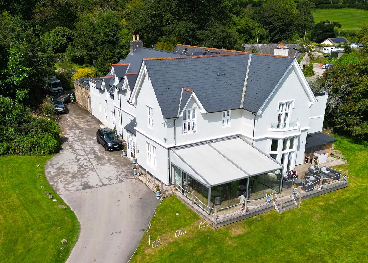An aerial view of a large white house with a gray roof surrounded by trees.