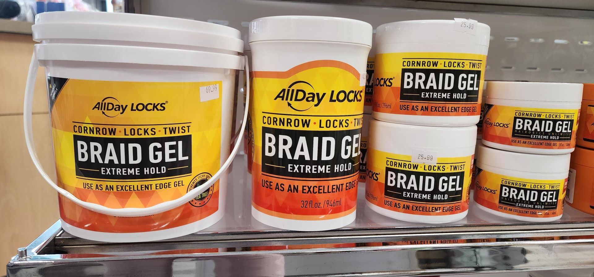 Containers of All Day Locks Braid Gel on a shelf. The containers are white with yellow and orange labels.