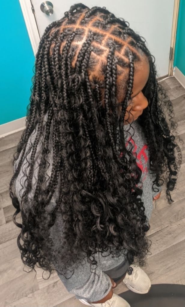 Top-down view of a person with long braided hair and curly ends, wearing gray clothes indoors.