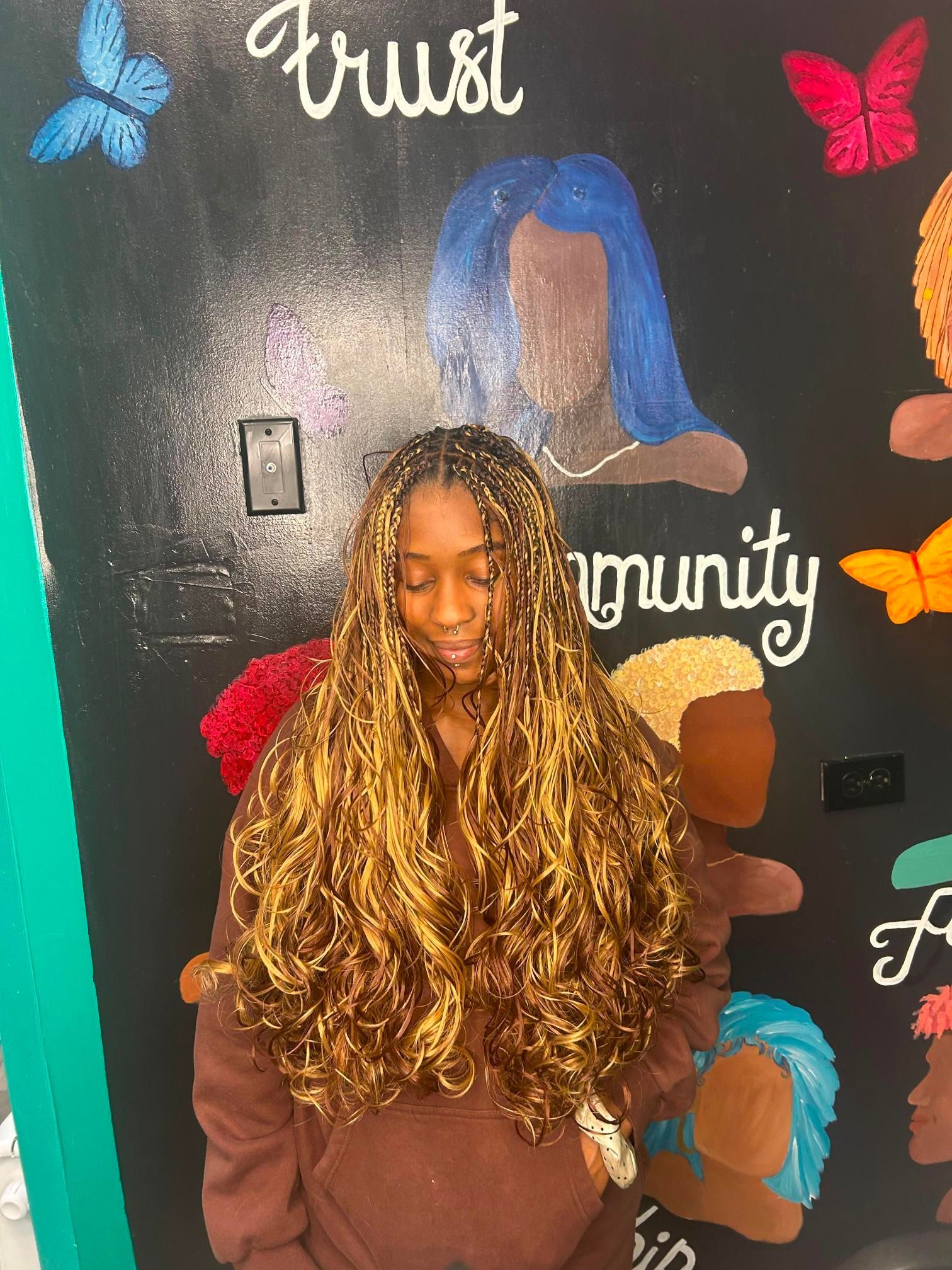 Person with long curly hair in a brown top, standing before a colorful chalkboard mural with butterflies.