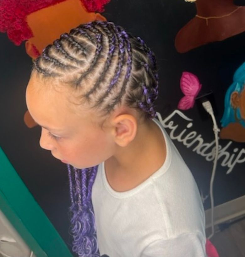 Child with purple braided hair in profile, wearing a white shirt, against a colorful wall with “friendship” sign.