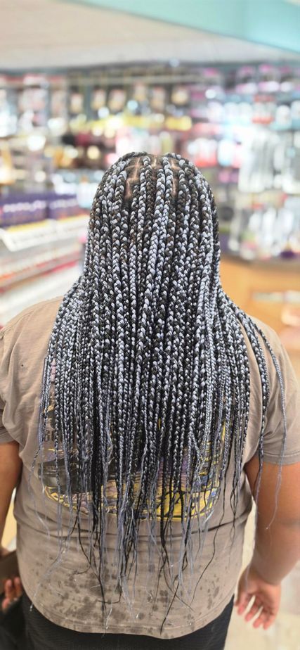 Person with long braided hair standing in a grocery store aisle, viewed from behind.