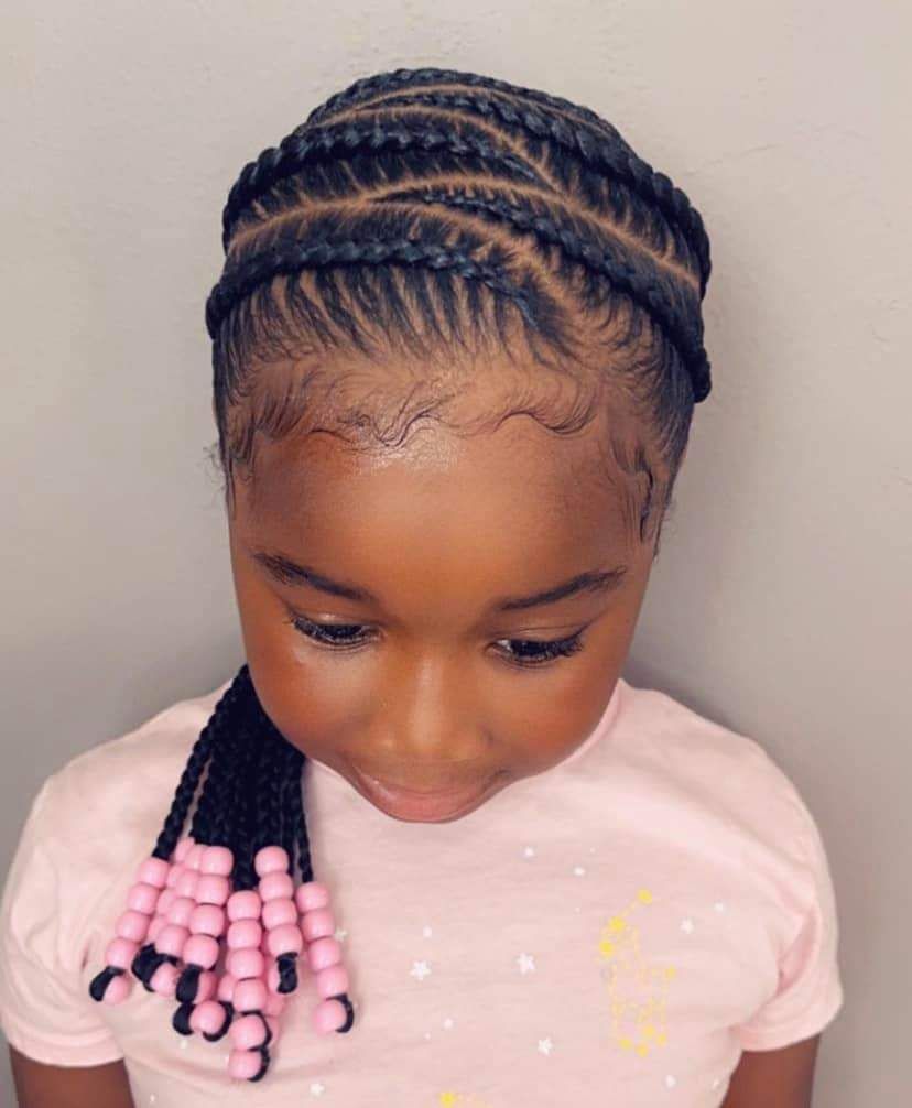 Child with braided hair and pink beads looking down, wearing a light pink shirt.