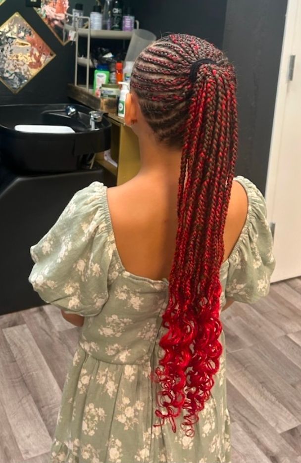 Person with long red braids in a green floral dress, seen from behind in a salon.