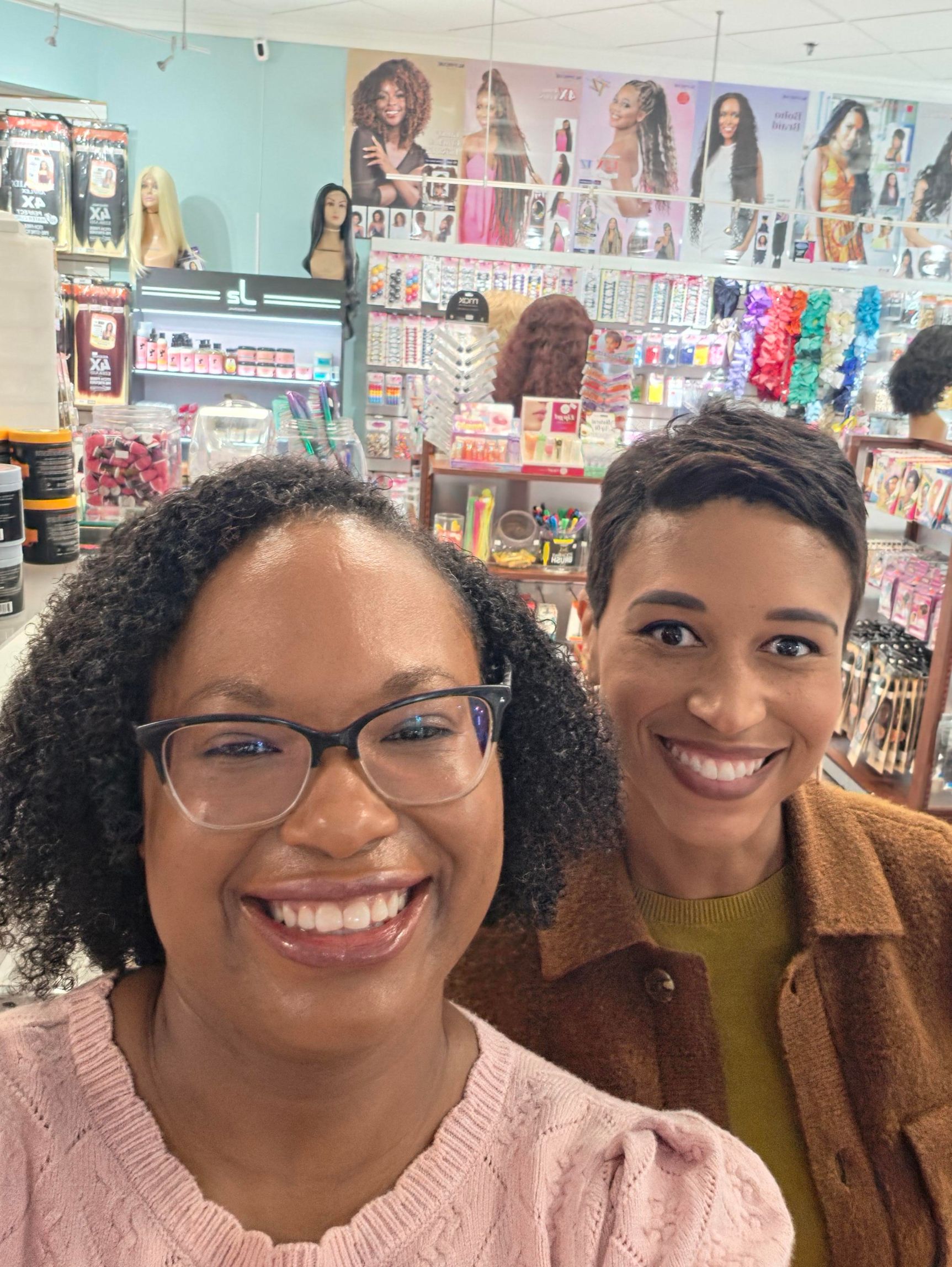Two smiling people in a colorful hair and beauty supply store, shelves filled with products behind them