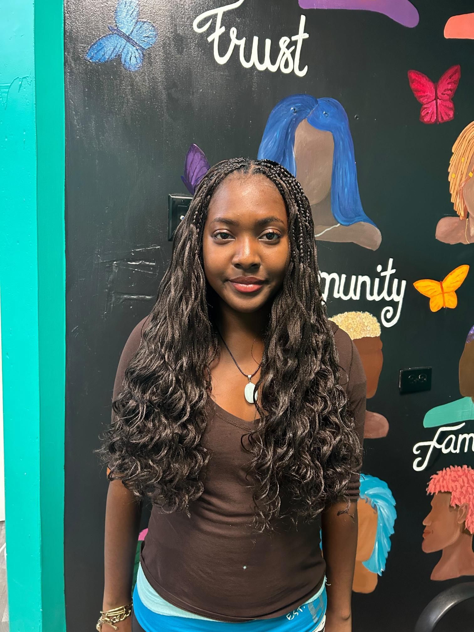Woman with long curly hair standing before a colorful mural with the words “Trust” and “Community” visible