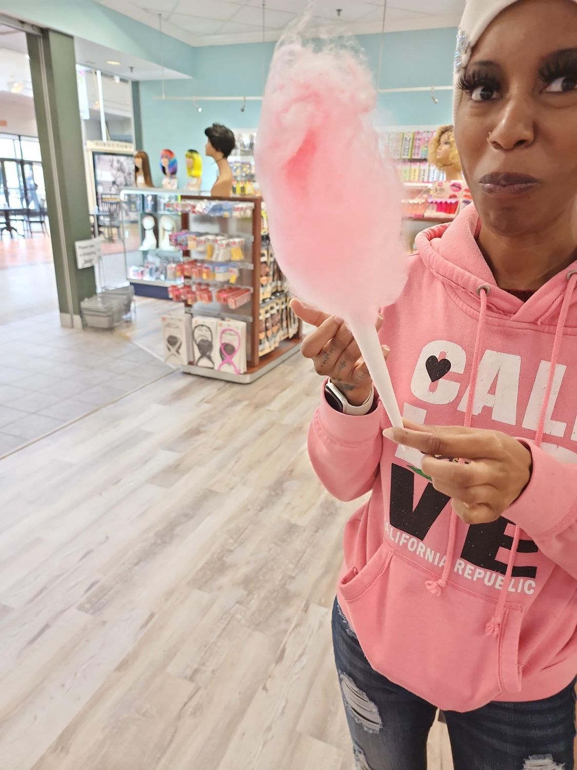 Woman in a pink hoodie holding pink cotton candy inside a bright candy store.