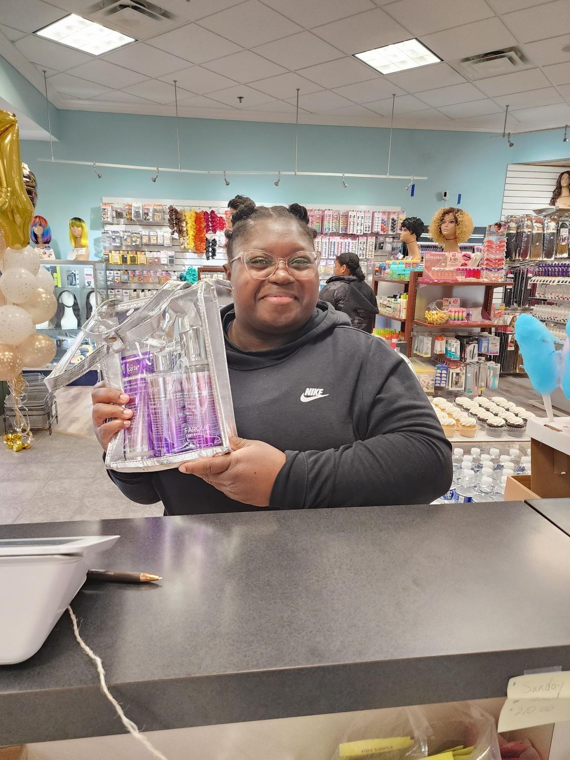 Person holding a wrapped gift basket in a shop, standing behind a counter.