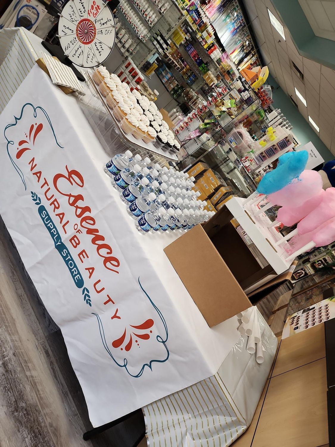 Vendor booth with cupcakes, water bottles, and a white tablecloth at an indoor event