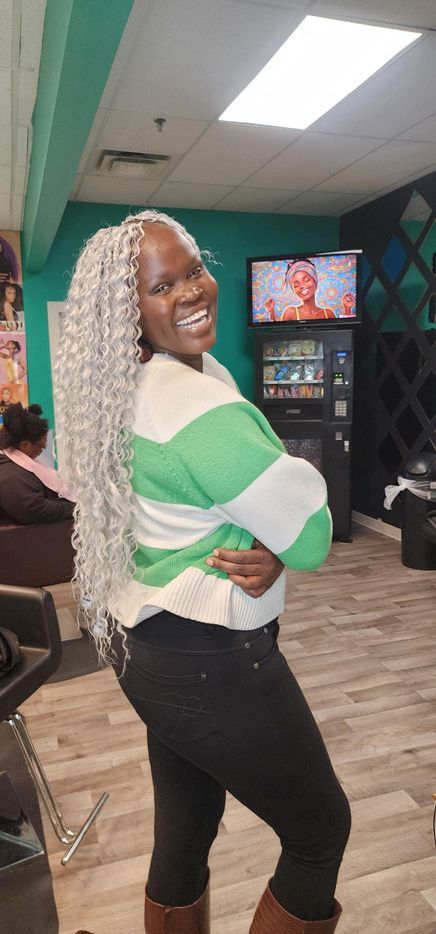 Smiling woman in a green-and-white striped top and black pants posing indoors with hand on hip