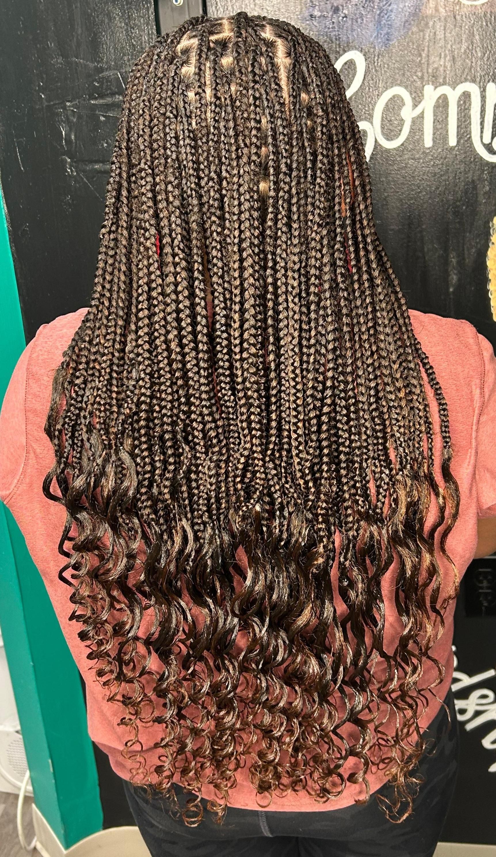 Back view of long braided hair with curled ends, wearing a pink top against a dark chalkboard wall.