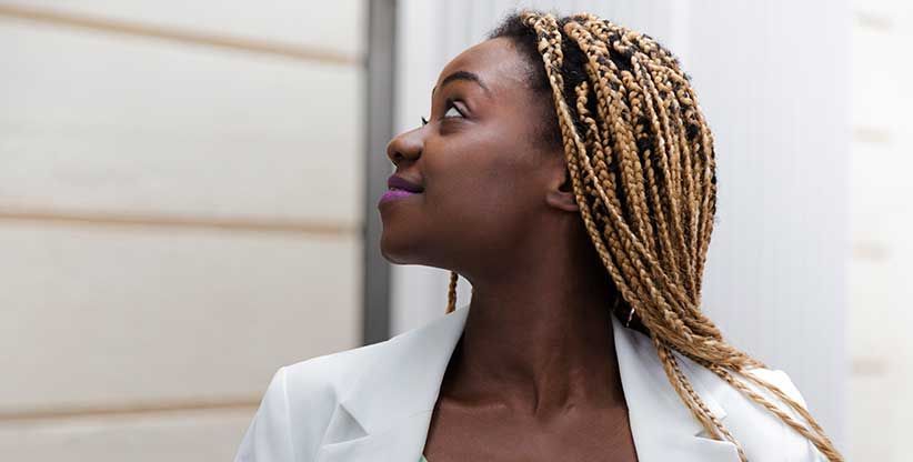 Black woman with blonde braids wearing a white blazer, looking up with a thoughtful expression.