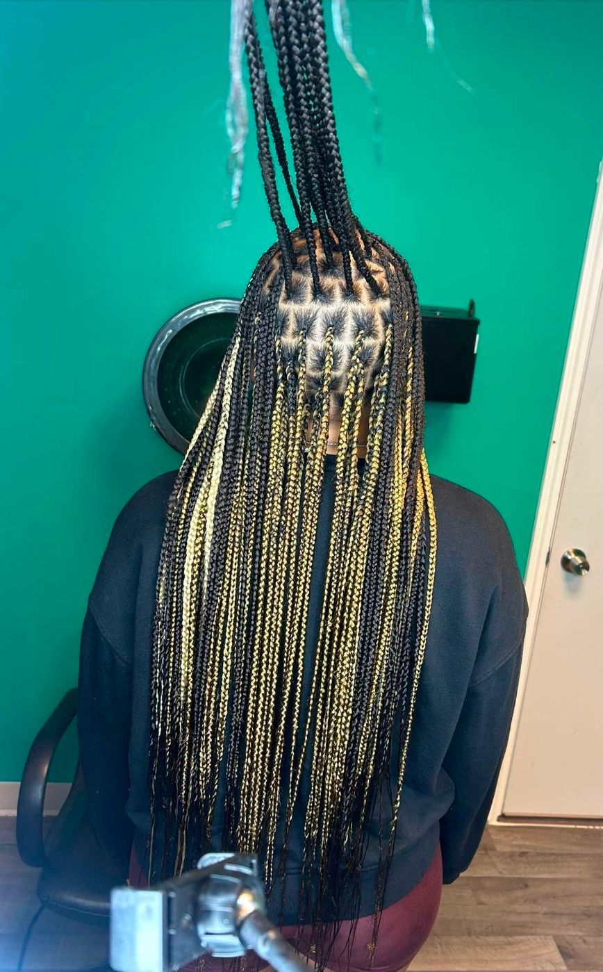 Person with long braided hair seated facing a teal wall, seen from behind.
