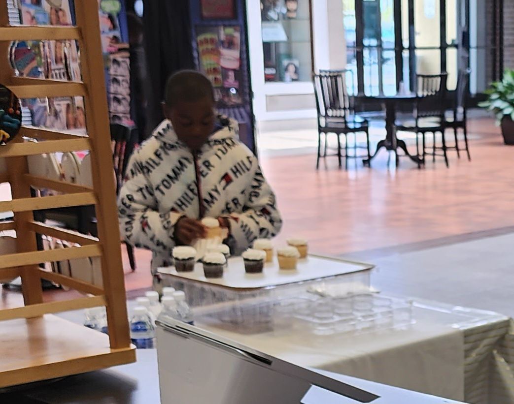 Person arranging small cups on a table in a bright indoor café or lobby area.