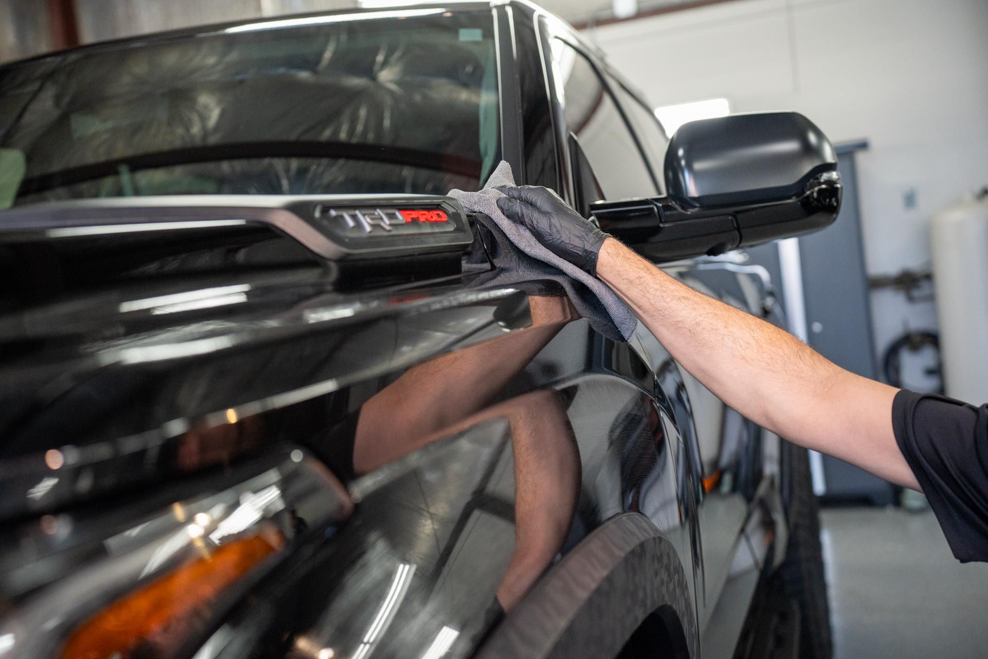 A man is cleaning a car with a cloth in a garage.