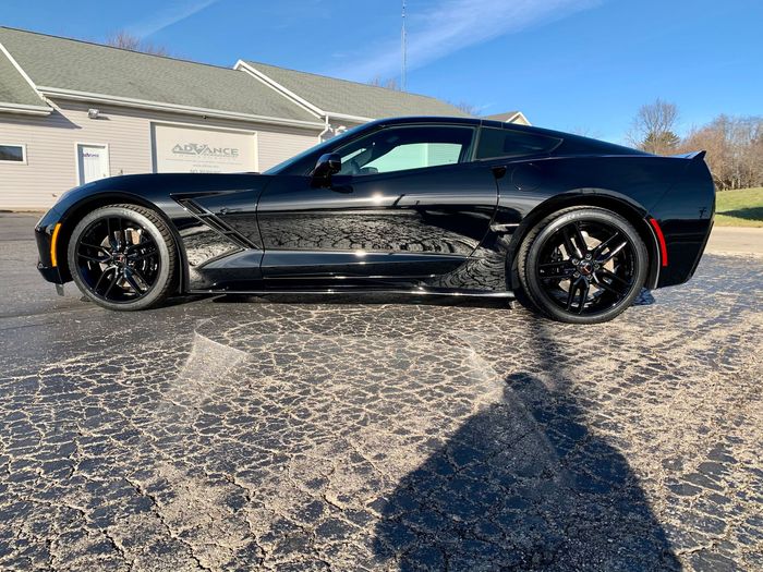 A black corvette is parked in a parking lot in front of a building.