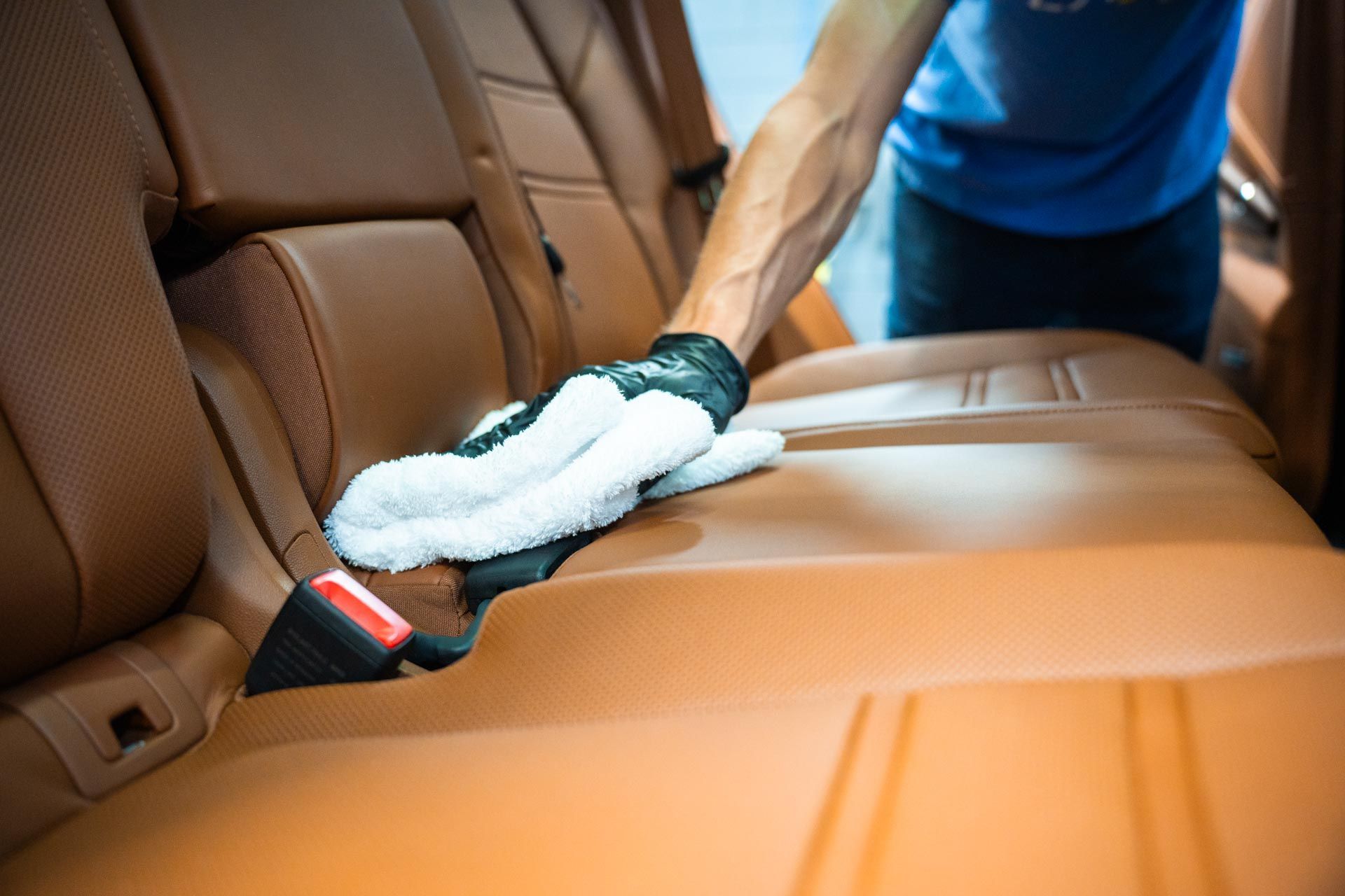 A man is cleaning the back seat of a car with a towel.