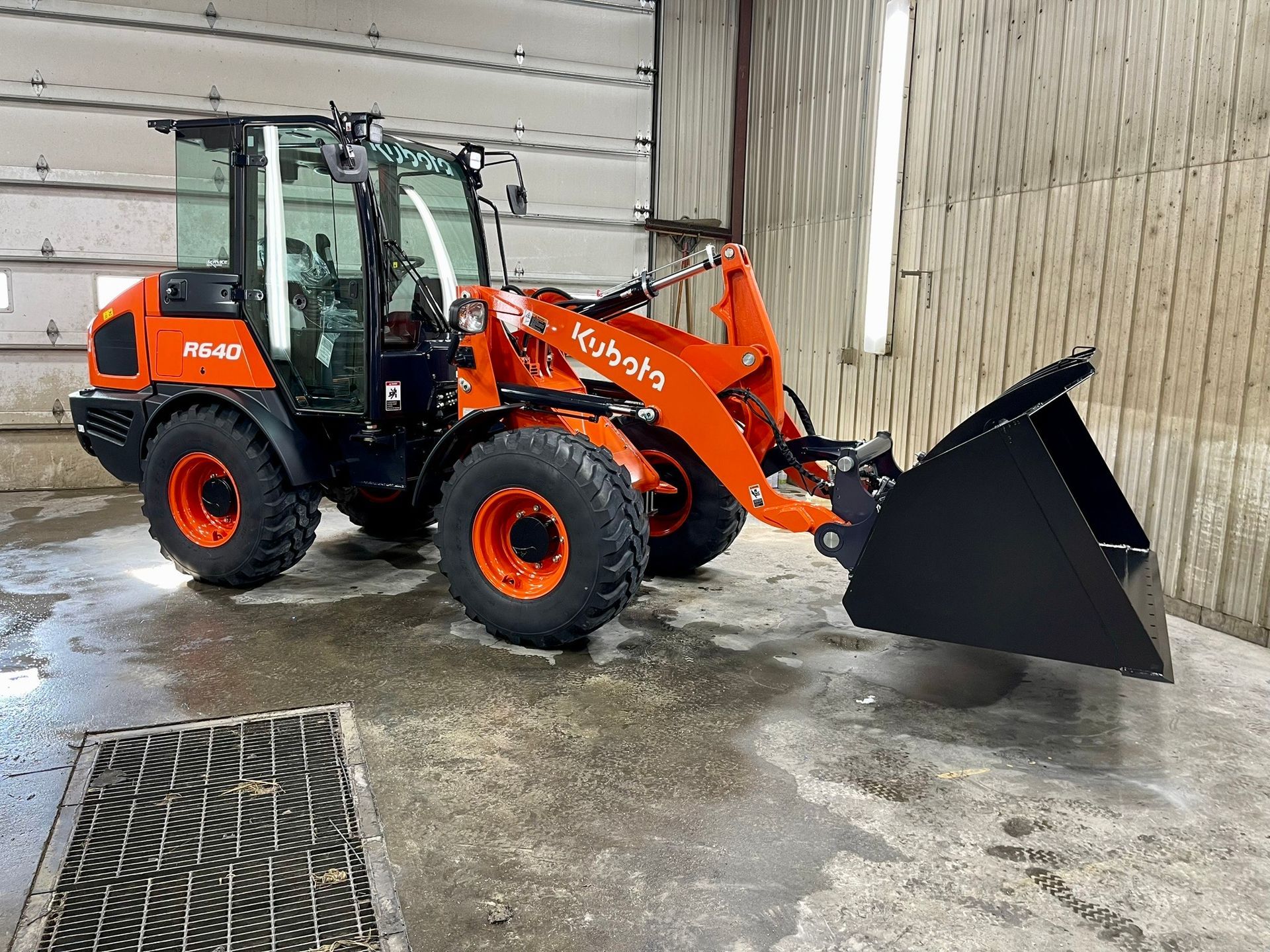 An orange and black tractor with a black bucket is parked in a garage.