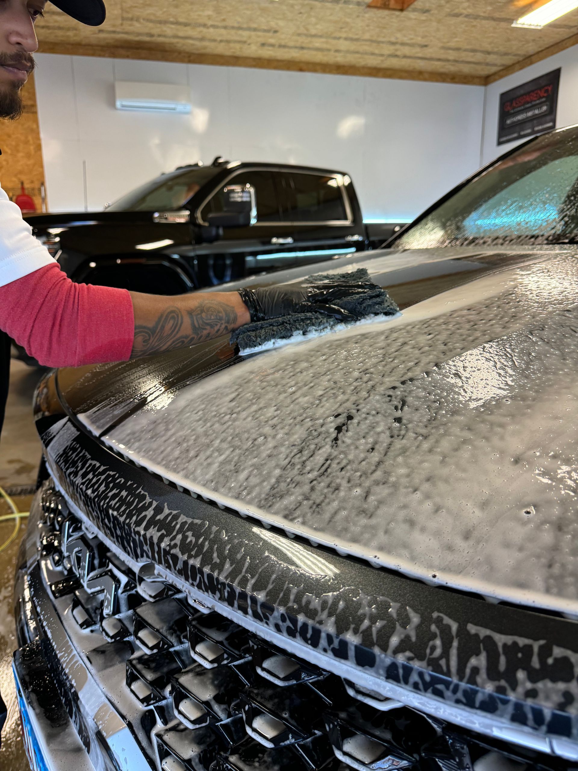 A man is washing the hood of a black truck in a garage.