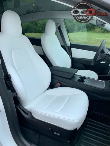 The interior of a white tesla model 3 with white seat covers.
