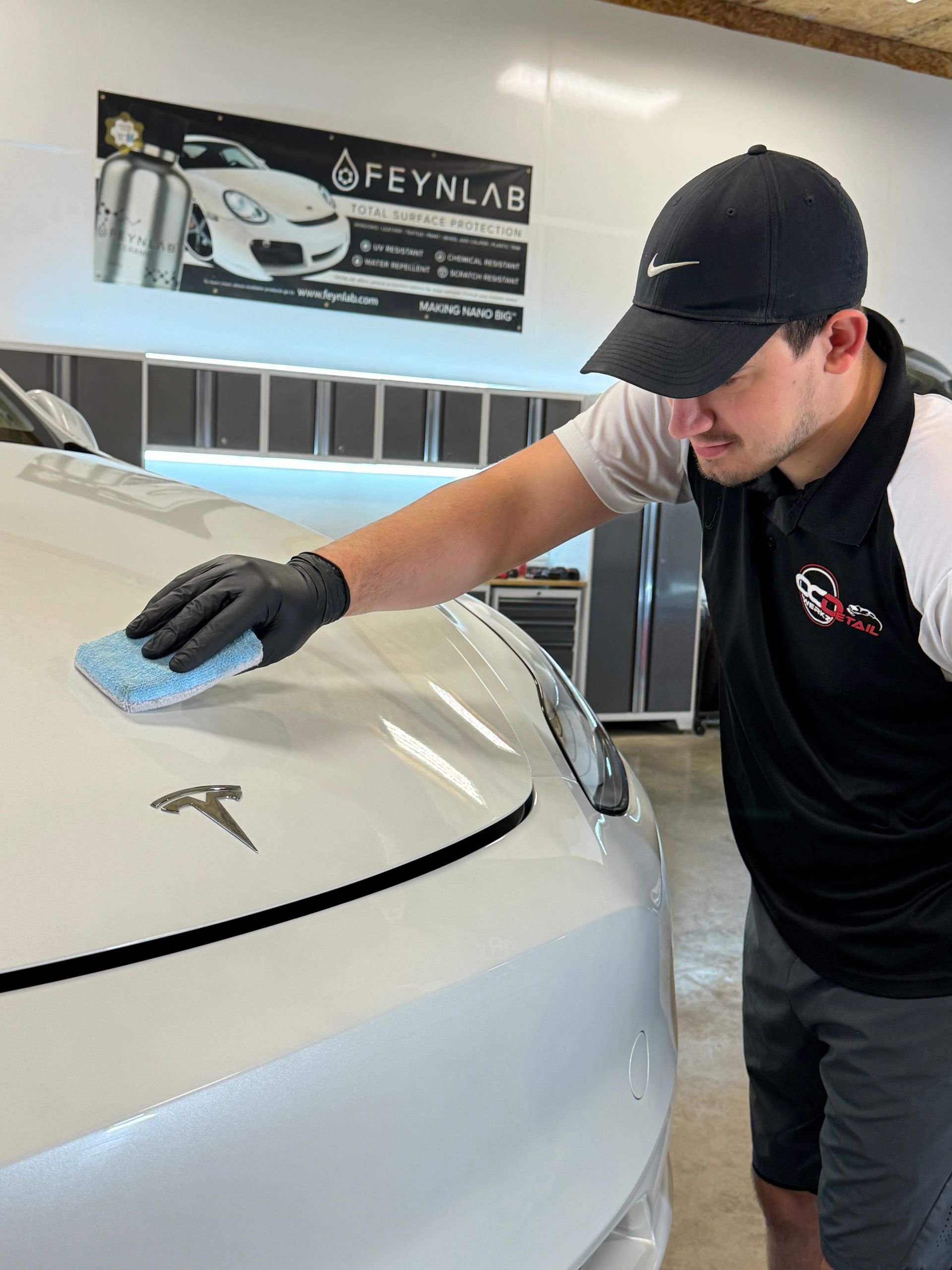 A man is cleaning the hood of a white tesla model 3.