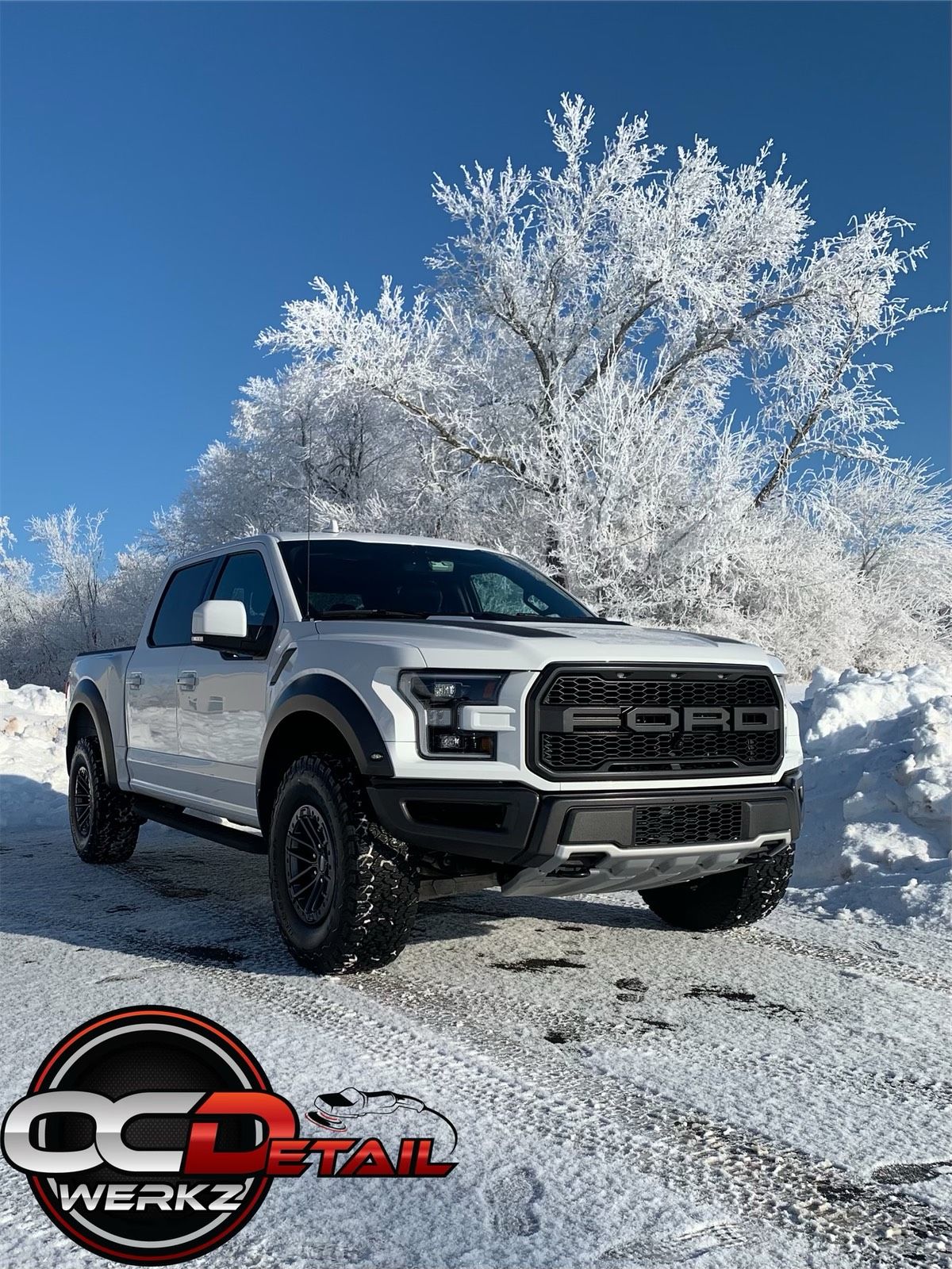 A white ford raptor is parked in the snow.