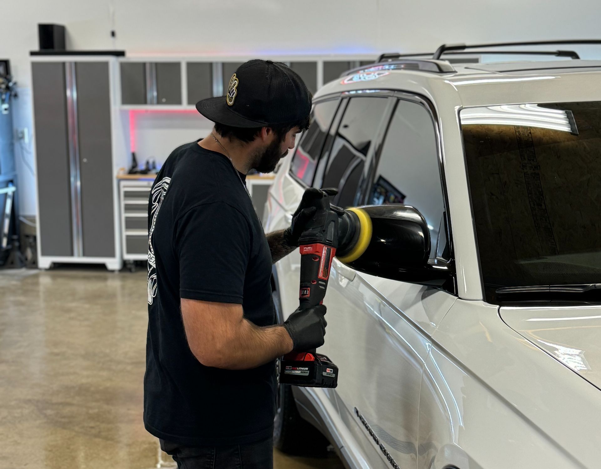 A man is polishing a white car with a machine.