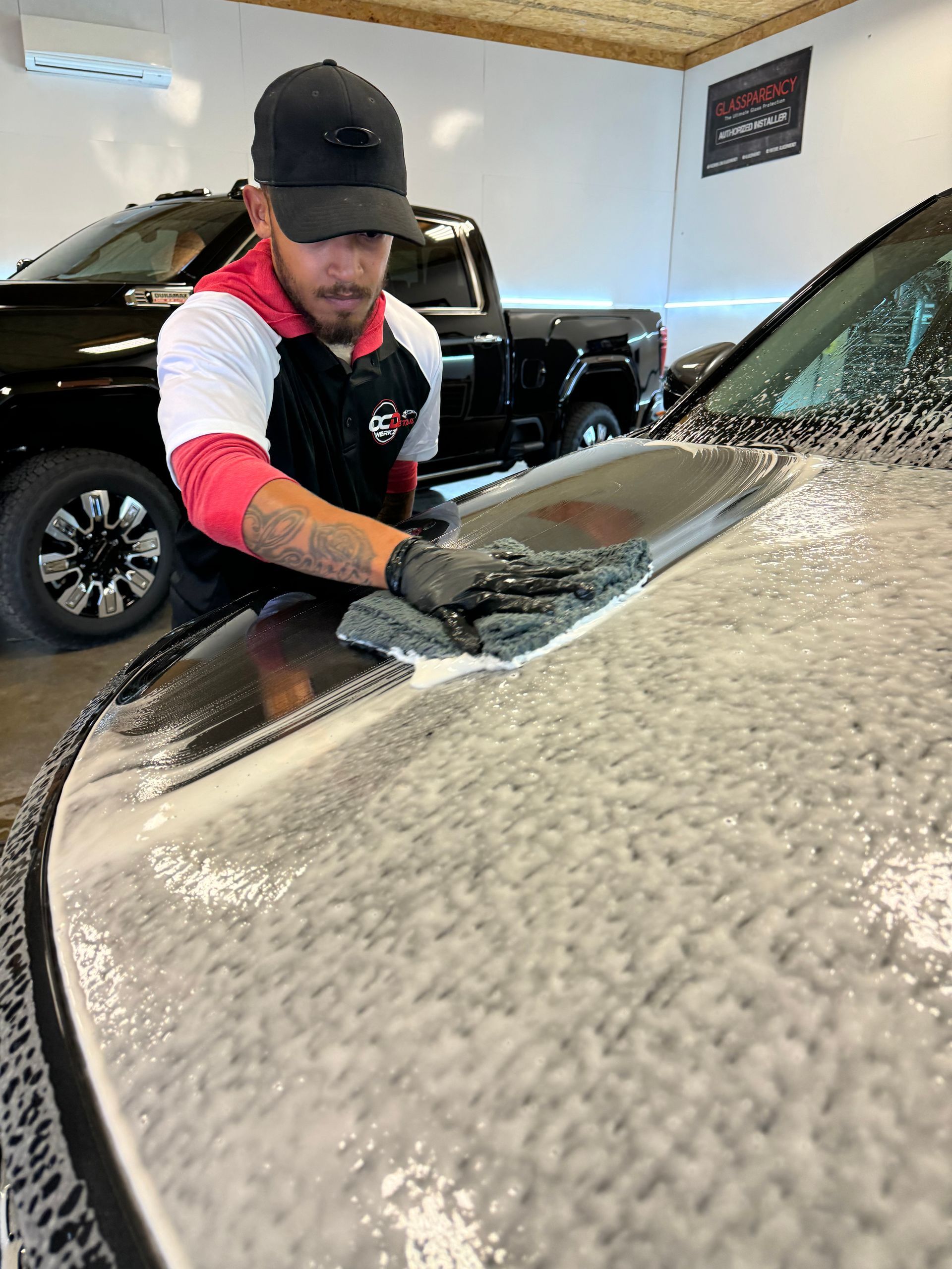 A man is cleaning the hood of a car in a garage.