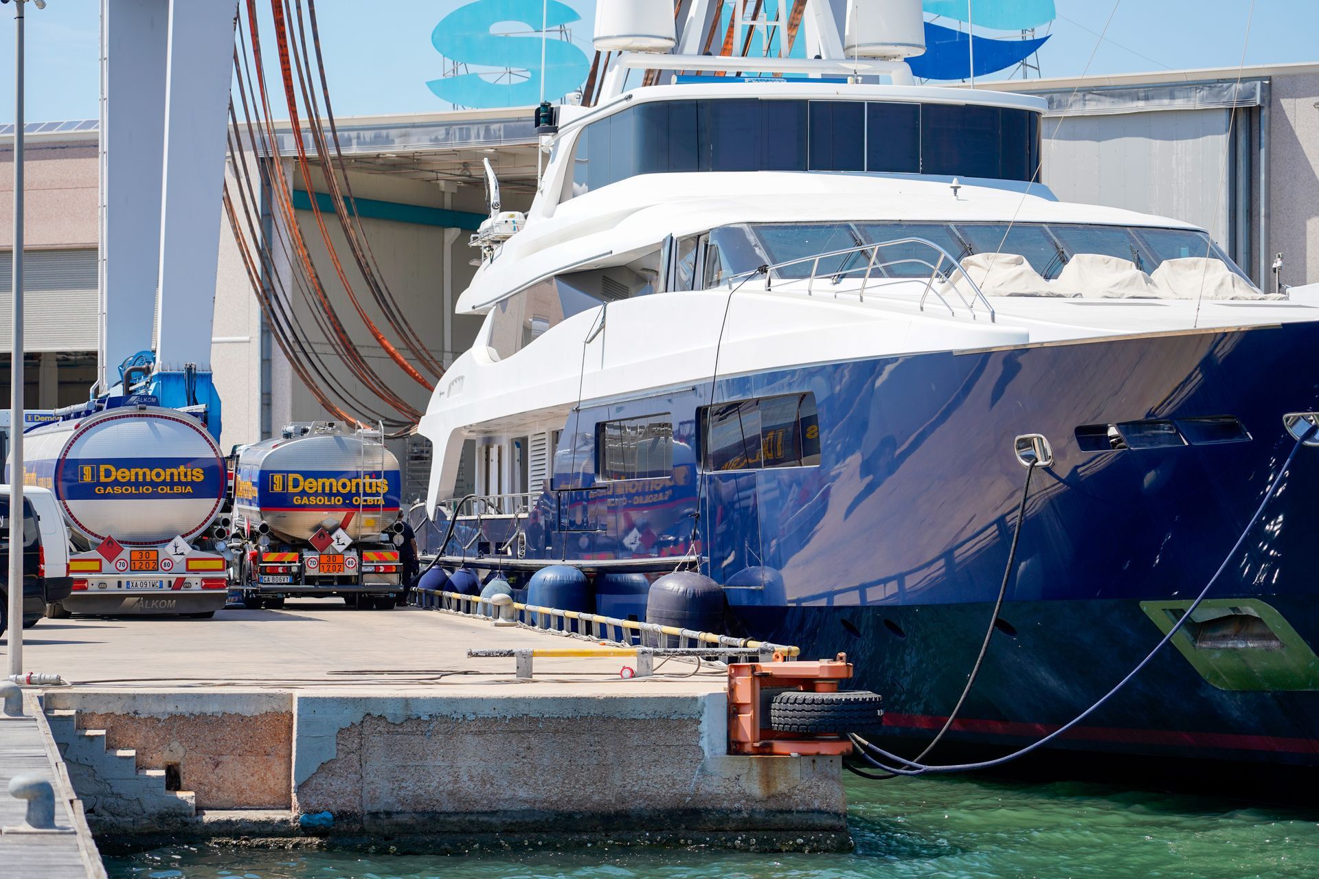 Un grande yacht blu e bianco è ormeggiato accanto a due rimorchiatori in un posto barca del porto turistico.
