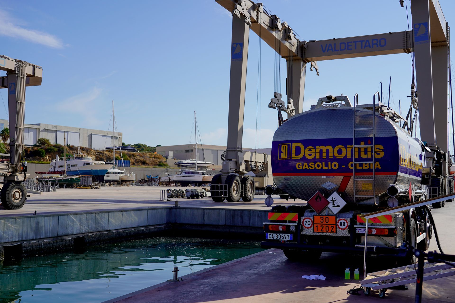 In una giornata di sole, una cisterna di carburante viene sollevata da una gru in un terminal portuale.