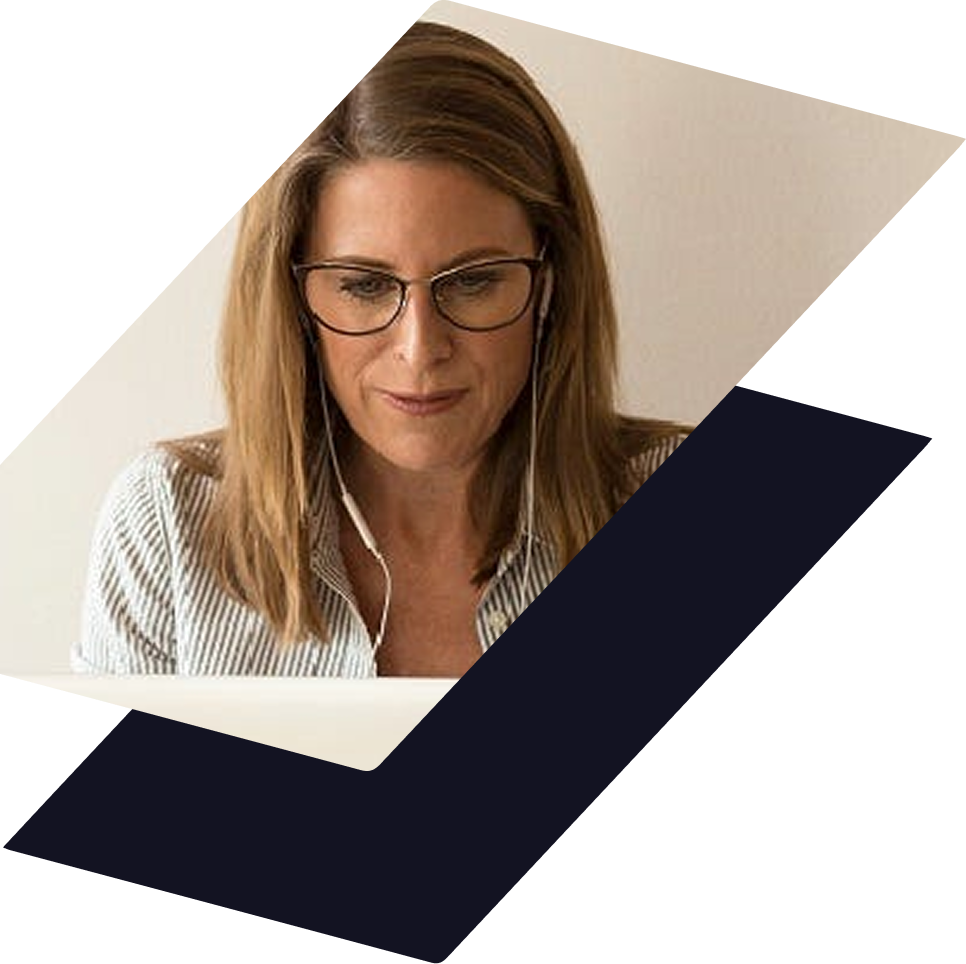 A person wearing glasses and wired earbuds looks down at a laptop screen against a light background.