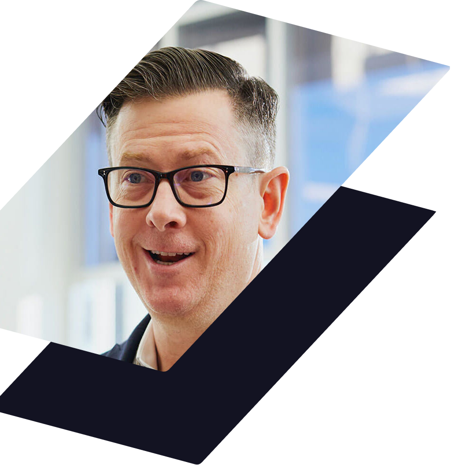 A person with short brown hair and dark-rimmed glasses smiling, set against a white and dark blue geometric background.