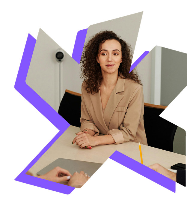 A person in a beige blazer sits at a table during a professional meeting, listening as others participate.