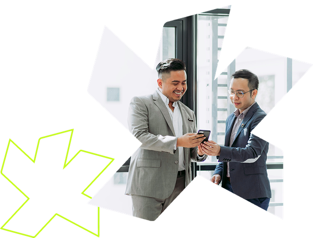 Two professionals in business attire smiling while looking at a smartphone in an office setting.