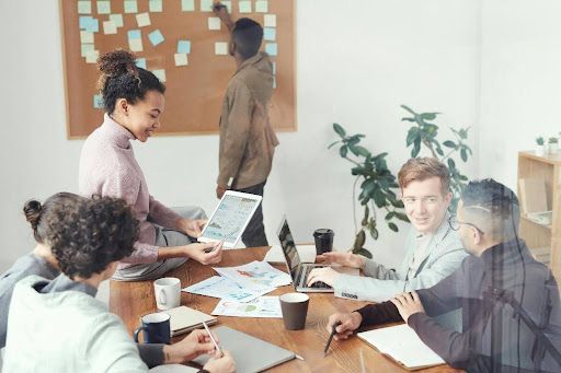 Group of people brainstorming around a table, one writing on a sticky note board.