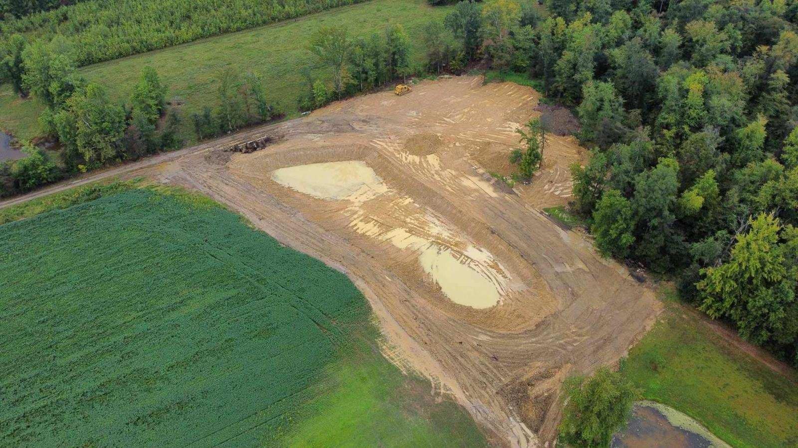 Aerial view of a cleared area near a forest and field; the cleared area has patches of standing water.