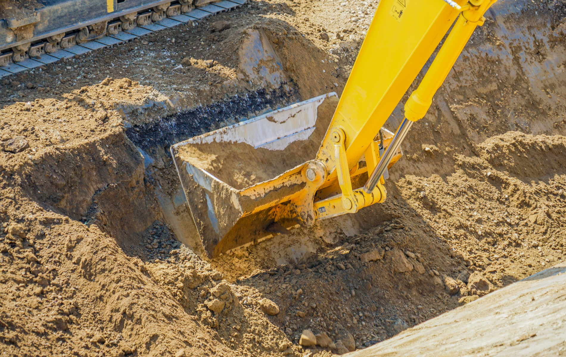 Yellow excavator bucket digging into brown earth.