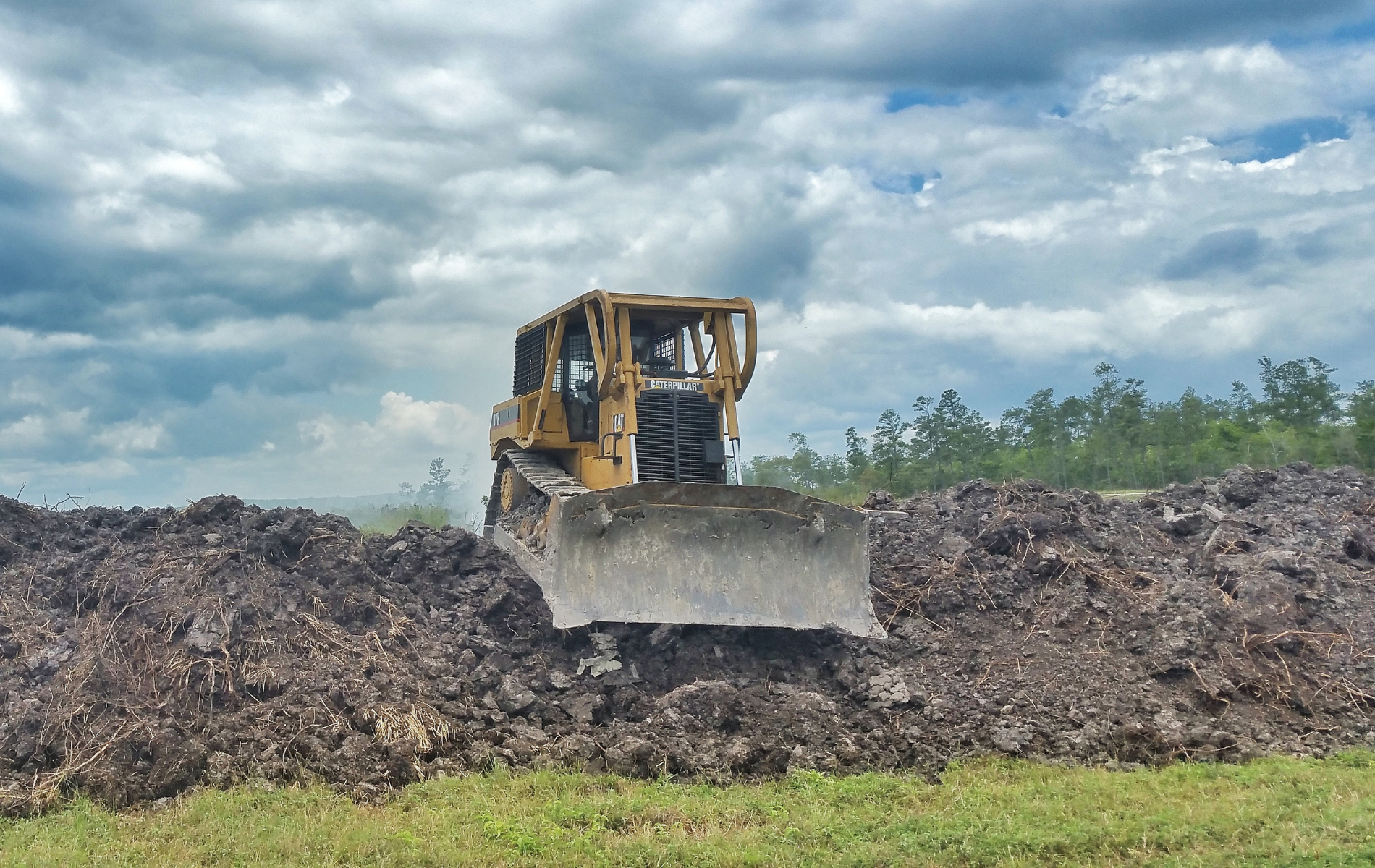 A yellow bulldozer pushing a large pile of dirt under a cloudy sky.