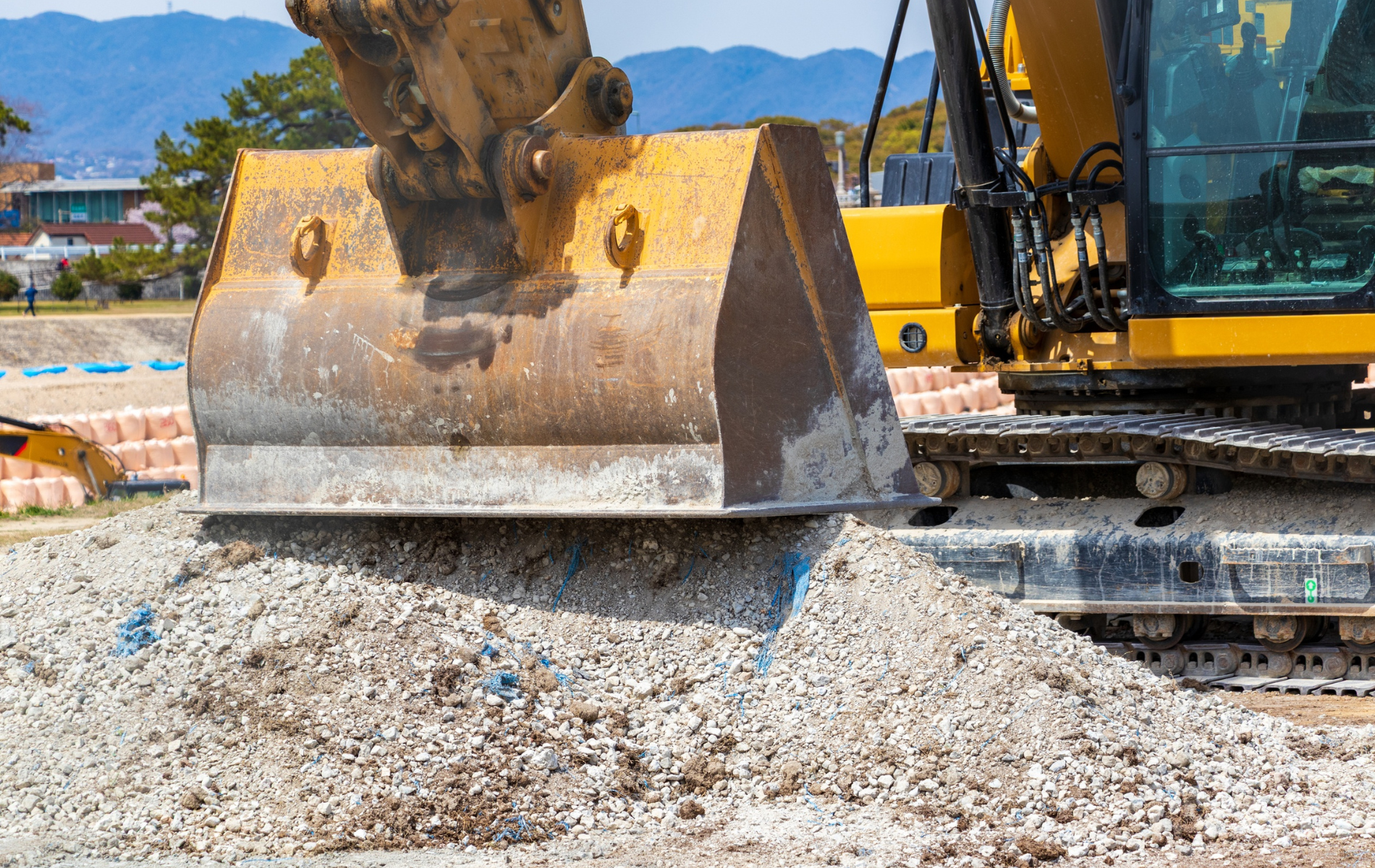 Yellow excavator bucket scooping up gravel at a construction site.