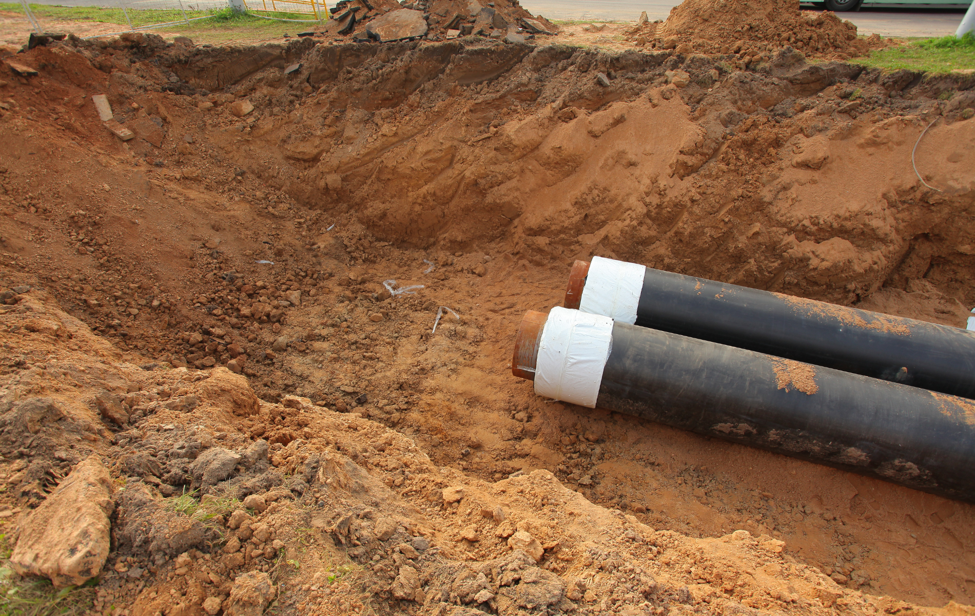 Two black pipes with white ends in a dirt trench, possibly for underground utility installation.