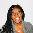 A woman wearing glasses and a grey sweater is smiling