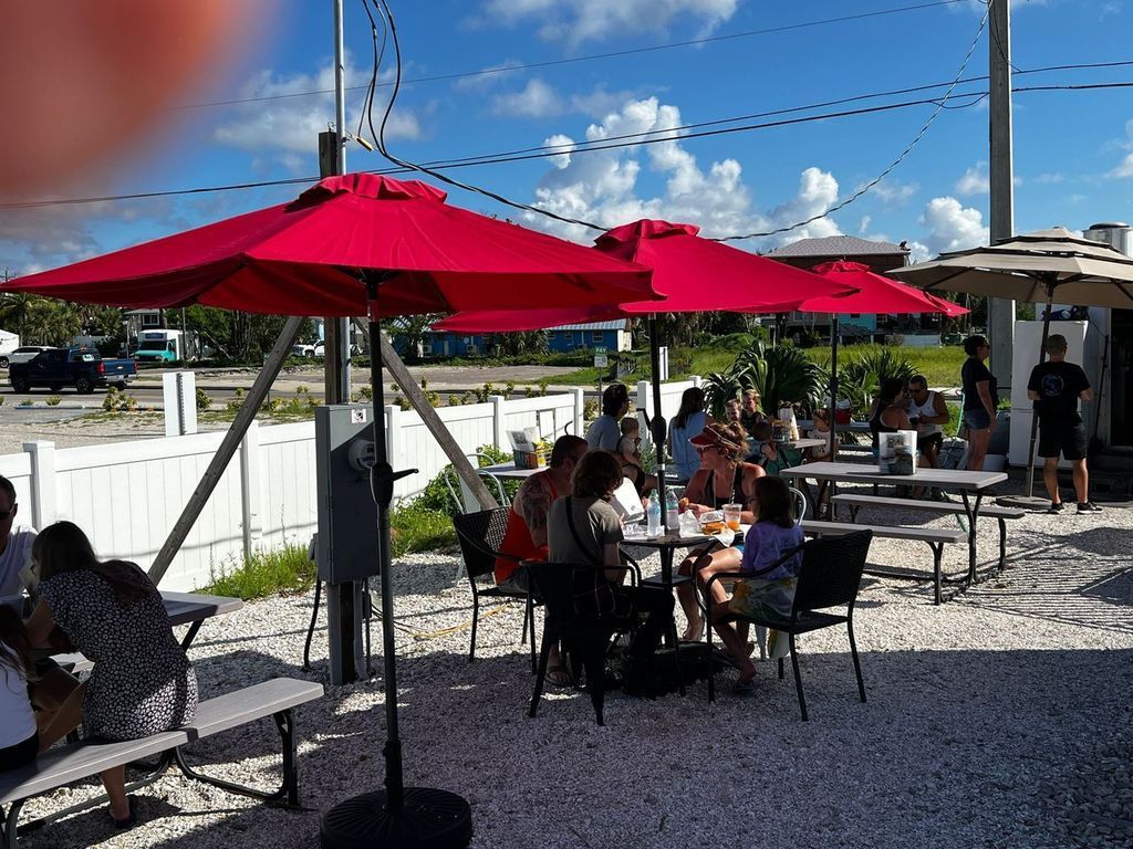 Outdoor dining area with red umbrellas, people seated at tables, bright sunlight.