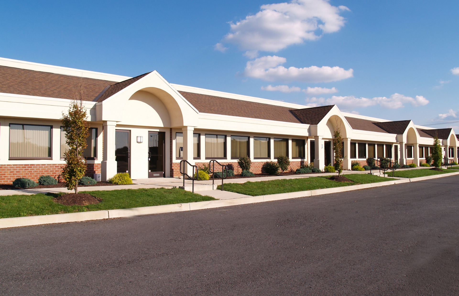 Row of beige townhouses with white arches and a paved street under a blue sky