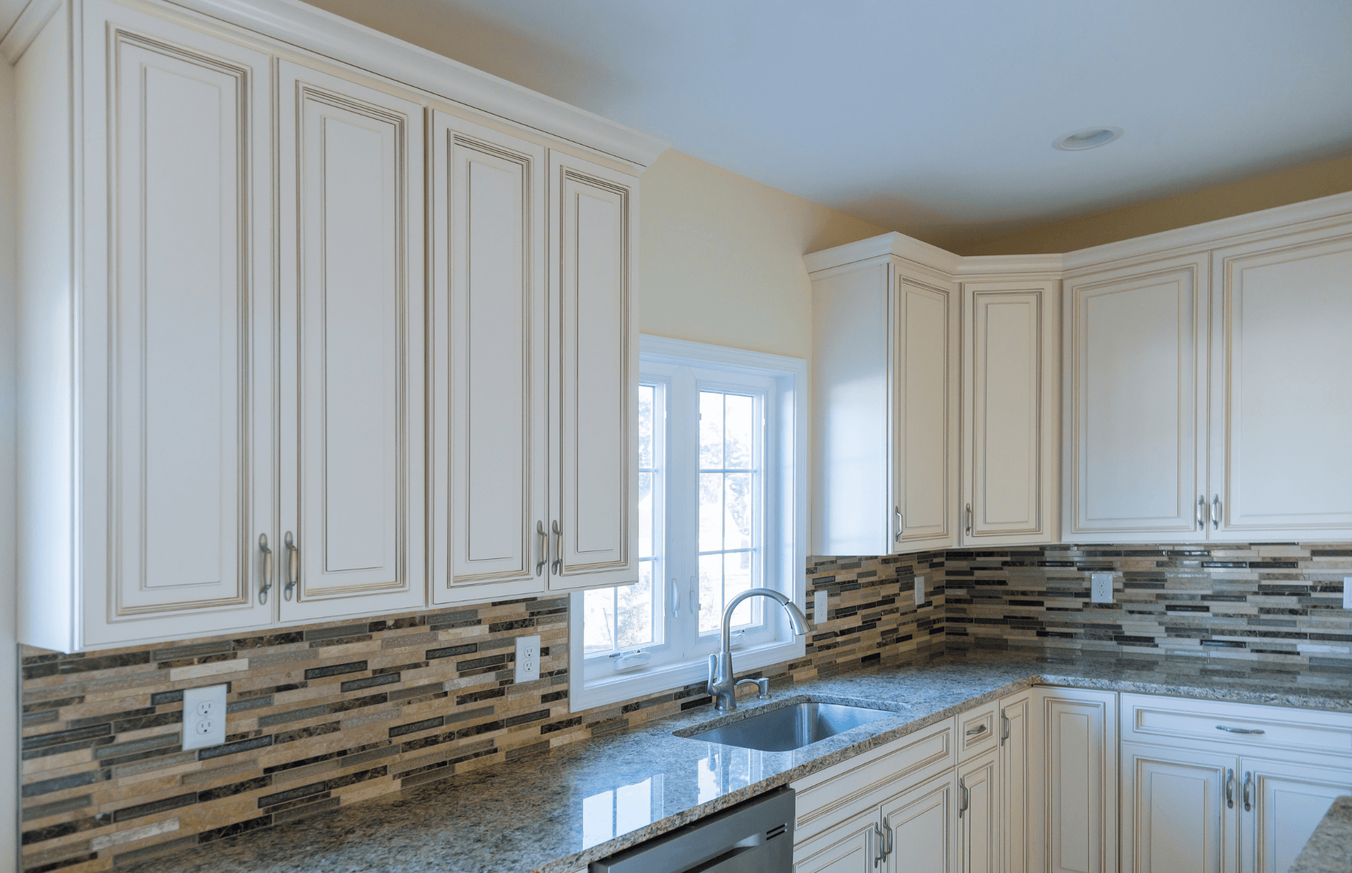 Bright modern kitchen with cream cabinets, mosaic backsplash, and a window over the sink.