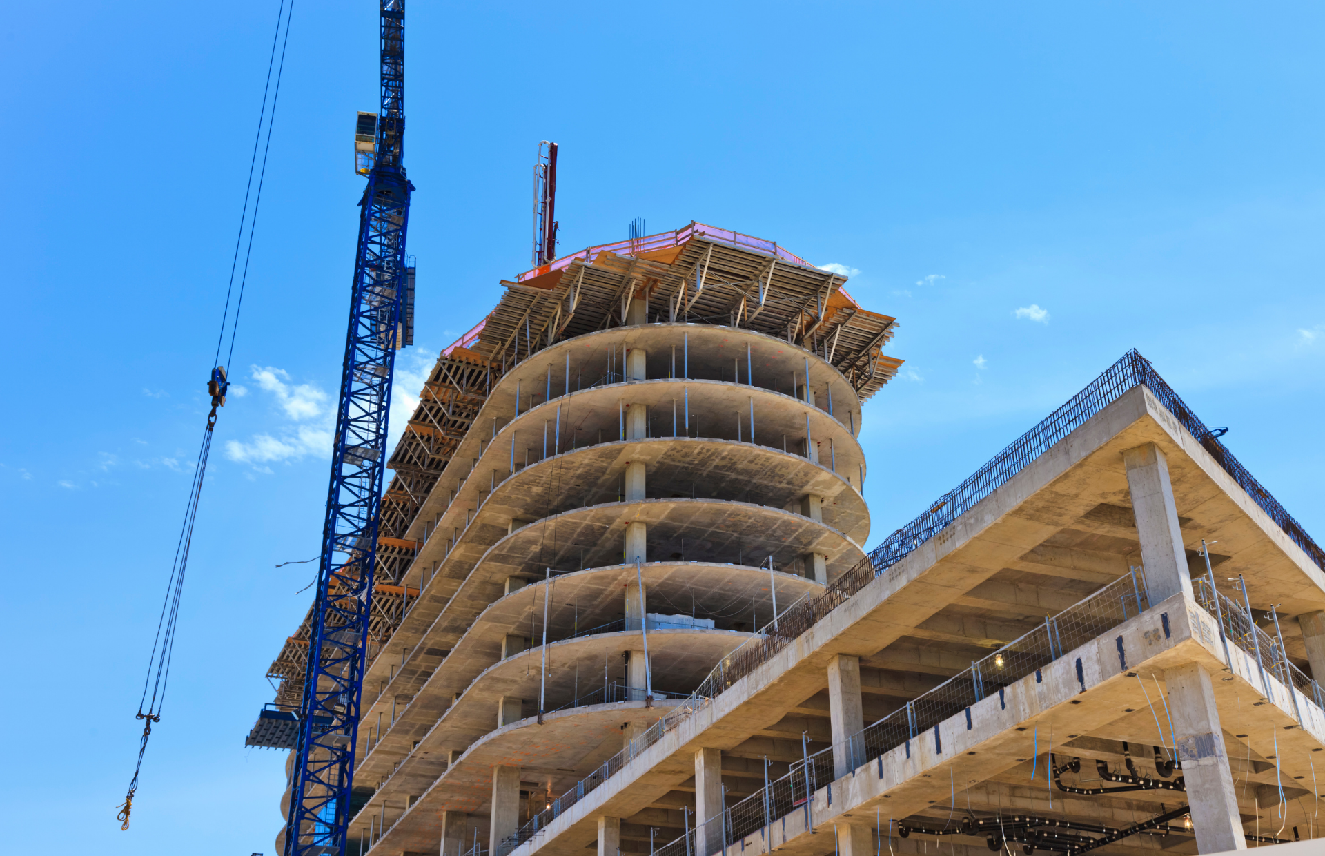 High-rise construction site with a blue crane and curved concrete tower against a clear blue sky
