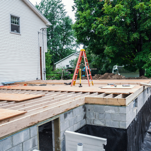 House under construction with wooden floor framing, cinder block foundation, and a red ladder on the deck