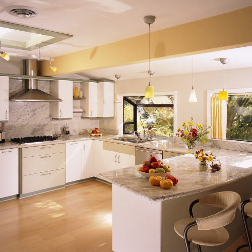 Bright modern kitchen with white cabinets, marble island, pendant lights, and fruit on the counter