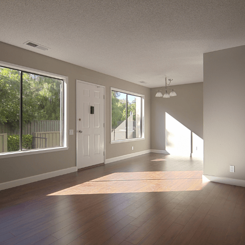 Empty sunlit living room with large windows, wood floors, and beige walls